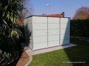 Ein moderner Gartenschuppen aus hellem Material, umgeben von Büschen und einer Grünfläche.