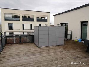Dachterrasse mit Holzboden, modernem Gebäude, grauem Schrank, Pflanzenkübeln und Gießkannen.