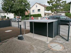 Ein modernes Gartenhaus in einem Vorgarten, umgeben von Zaun, mit Straße und Autos im Hintergrund.