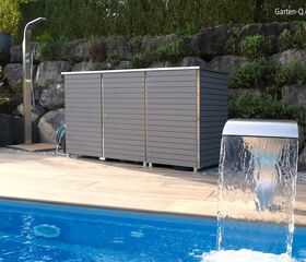 Ein moderner Poolbereich mit Wasserfall, grauem Gartenhaus, Außendusche, Pflanzen und einer Steinmauer im Hintergrund.